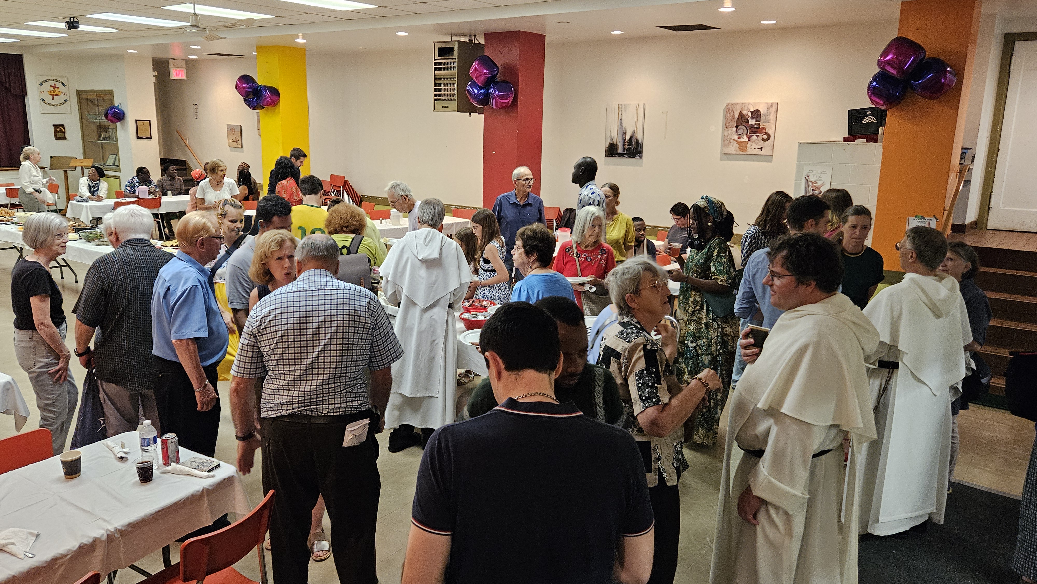 A parish hall where people are talking, drinking, and eating food